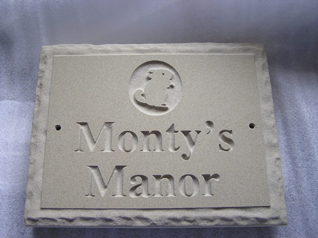 A stone carved plaque with the words, "Monty's Manor" and a chinchilla engraved into it.
